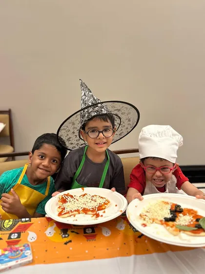 Three happy chefs showing off their finished Halloween pizzas. Each one is a unique creation, ready for the oven.