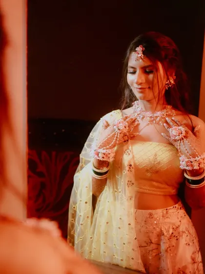 A bride's quiet moment of reflection before her Haldi ceremony. The warm, reddish light and the mirror view create a soft, intimate, and slightly mysterious portrait.