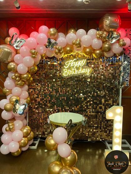 The full view of the pink and gold first birthday decoration. The combination of the shimmer wall, neon sign, and marquee number creates a glamorous and festive look.