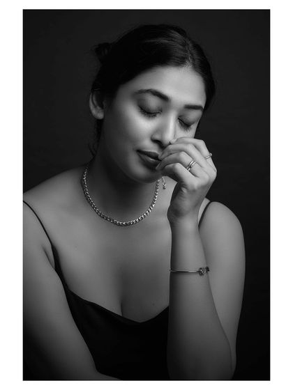 A contemplative black and white portrait. The model's pose and the soft lighting create a sense of quiet introspection and vulnerability.