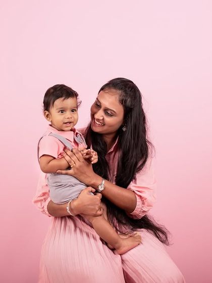 A mother and her baby against a soft pink backdrop. This classic portrait highlights the gentle bond and interaction between them.