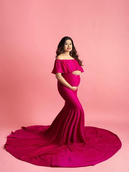 A full-length shot of a mom-to-be in a vibrant magenta gown against a matching pink backdrop. The off-the-shoulder dress flows beautifully, creating a bold and modern maternity photo.