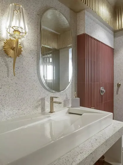 A close-up of the powder room vanity, showing the elegant wall sconce and the mix of textures between the terrazzo, tile, and metallic ceiling.