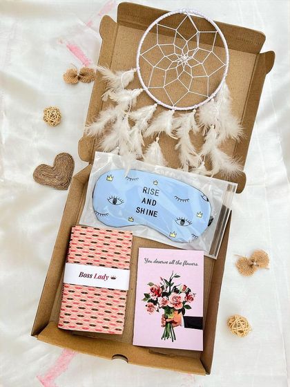 A thoughtful gift box designed for relaxation and good vibes. This hamper contains a white dream catcher, a "Rise and Shine" eye mask, a "Boss Lady" journal, and a beautiful greeting card.