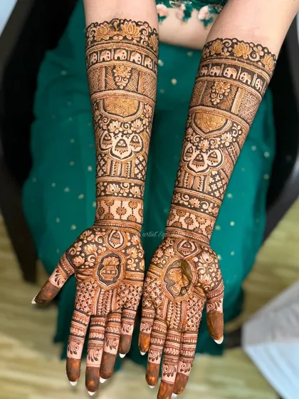 This bridal design is filled with traditional elements, including elephant motifs, hanging bells (jhumkis), and detailed portraits, telling a complete story on the arms.