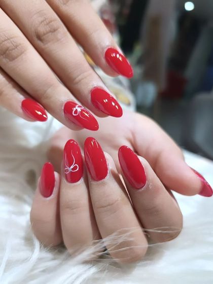 A simple yet bold design with glossy red nails and delicate, hand-painted white bow outlines on accent nails.