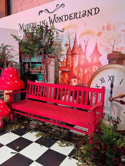 'Mishri in Wonderland,' a whimsical party theme with a giant storybook backdrop, a massive clock, and a bright red bench for photos.
