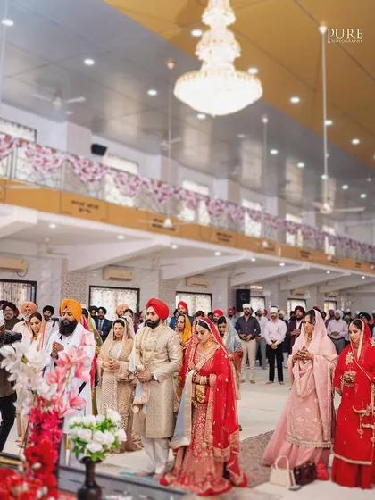 A wide shot of the Anand Karaj ceremony, showing the couple and their families gathered in the Gurdwara hall. It captures the scale and community feel of the event.
