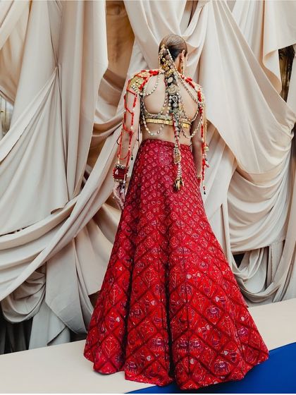 A full-length view of the bride in her red lehenga, showcasing the magnificent jewelry-adorned braid. This shows how a statement hairstyle can be the centerpiece of a bridal look.