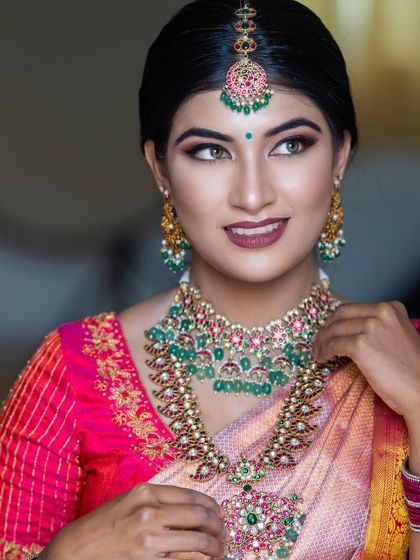 A close-up shot that captures the detail of the eye makeup and the beautiful emerald and ruby jewellery.