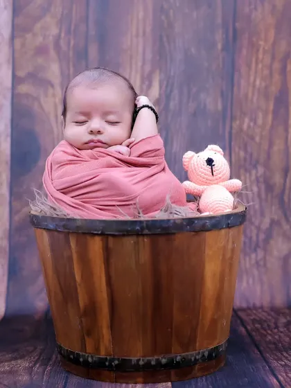 A classic newborn pose, with the baby swaddled and sleeping soundly in a rustic wooden bucket. This highlights their tiny, curled-up form perfectly.