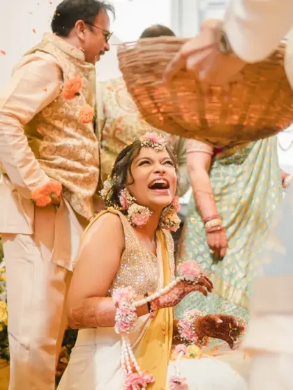 The bride laughs with delight as a basket of flower petals is showered over her. This shot is overflowing with the joy and festive spirit of the Haldi ceremony.
