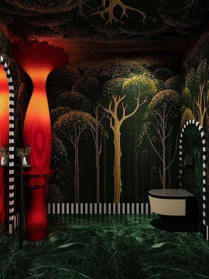 An enchanted forest-themed powder room, with dark green marble, tree-patterned wallpaper, and dramatic red sculptural elements.