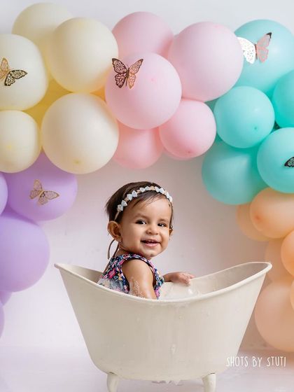 The full setup for the splash session, with pastel balloons decorated with butterflies. The theme continues from the cake smash to the bath for a cohesive gallery.