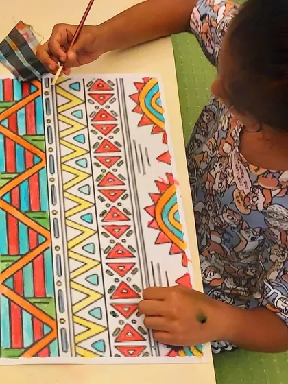 A student works on her vibrant African ethnic pattern painting, carefully filling in the designs with watercolor.