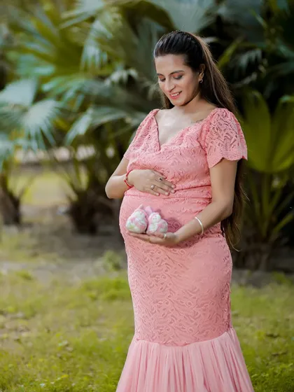 A quiet moment of anticipation. This mom-to-be looks down at a tiny pair of baby shoes, surrounded by the lush greenery of a park, creating a peaceful and emotional outdoor portrait.