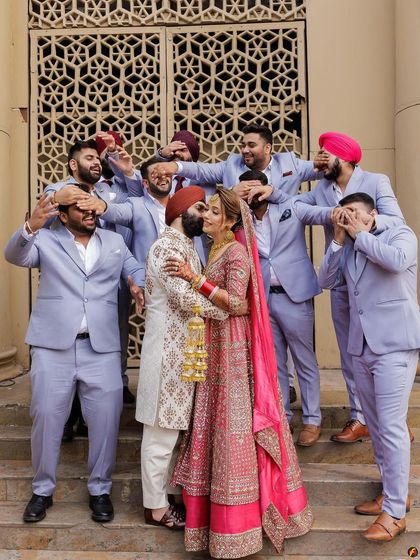 A playful take on a wedding portrait, with the groomsmen covering their eyes as the couple shares a kiss.