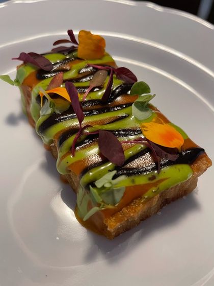 A savory bite served on a crispy toast base, artfully drizzled with two different sauces and garnished with microgreens.