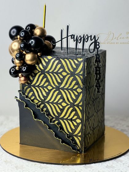 A modern, hexagonal black and gold cake. We used a stencil to create the intricate gold pattern, and the cake is topped with a balloon-like cluster of chocolate spheres.