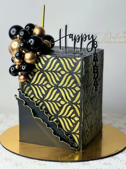 A modern, hexagonal black and gold cake. We used a stencil to create the intricate gold pattern, and the cake is topped with a balloon-like cluster of chocolate spheres.