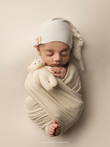 Cute little teddies. This newborn is swaddled in cream with a matching sleepy hat and a tiny bear, creating a dreamy and adorable scene.
