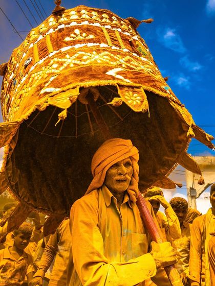 A devotee carries a large, decorated umbrella during the Vittal Birdev Yatra in Pattan Kodoli. The entire scene is drenched in golden turmeric powder, creating a surreal and vibrant atmosphere.