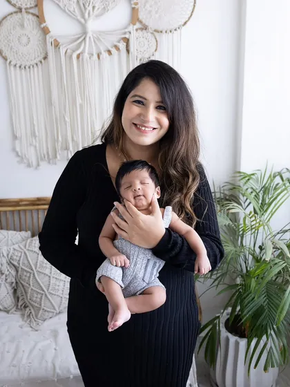 A beautiful portrait of a mother holding her newborn. The baby is dressed in a cute little outfit, and the mother's proud smile says it all.