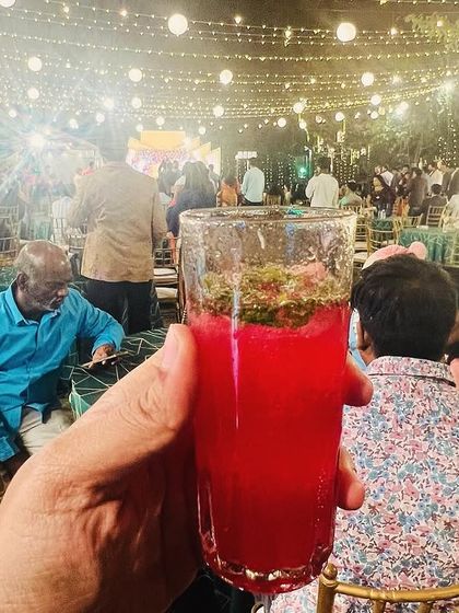 A guest holding a colourful mocktail against the backdrop of a beautifully lit evening event. My mocktail bar adds a splash of colour and refreshment to the party.