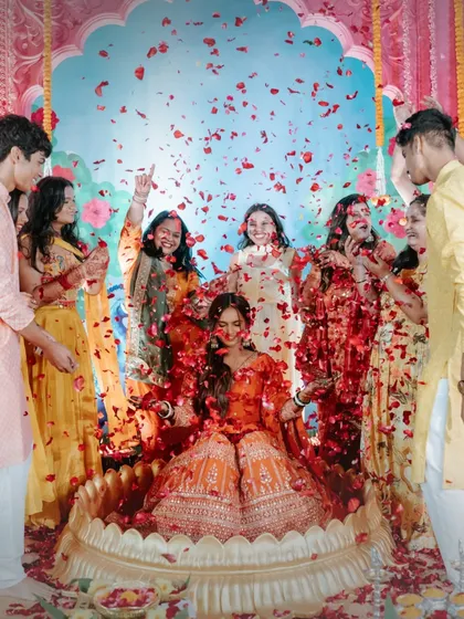 A joyous 'Phoolon ki Haldi' for the bride. She is surrounded by her friends and family as they shower her with red rose petals, creating a beautiful and memorable moment of celebration.