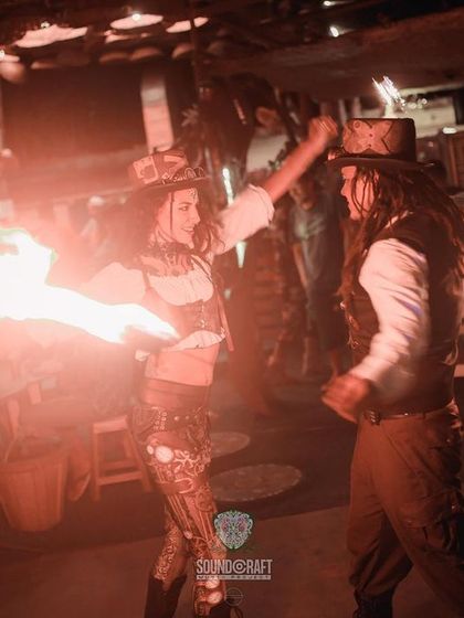 The Steampunk duo performs a fire act together. This image captures a moment of interaction between the two artists during their choreographed routine.