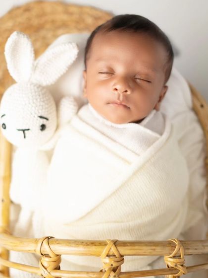 A close-up of the newborn's face, swaddled in white and sleeping next to a knitted bunny. This highlights the peacefulness of a newborn session.