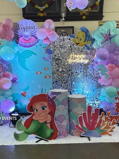 A close-up of the mermaid-themed stage, highlighting the pastel balloon arch and life-sized cutouts of Ariel, Sebastian, and a seahorse.