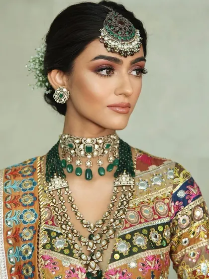 A close-up of a modern bridal look with a multi-coloured blouse. The makeup is soft and romantic, with a focus on a warm, peachy glow.