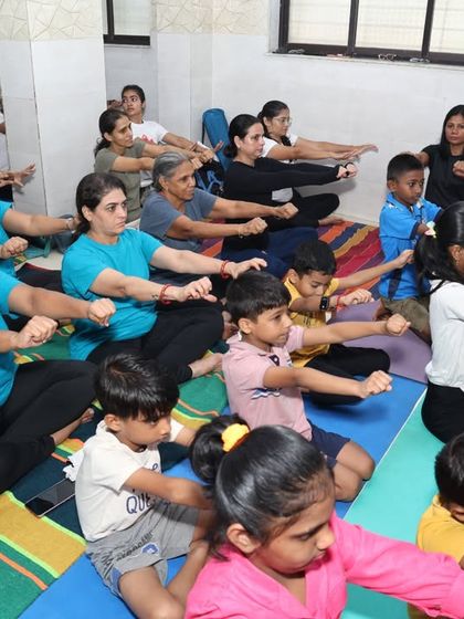 A full class of adults and children practicing arm stretches together during our International Yoga Day celebration. Our studio is a space where all ages can come together to learn and grow.