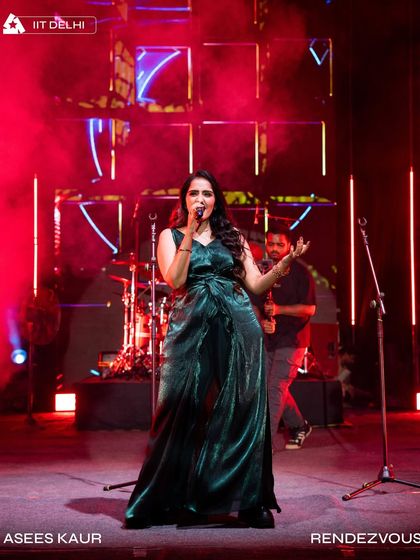 Asees Kaur performing at Rendezvous, IIT Delhi. The stage design featured unique geometric panels and red accent lighting.