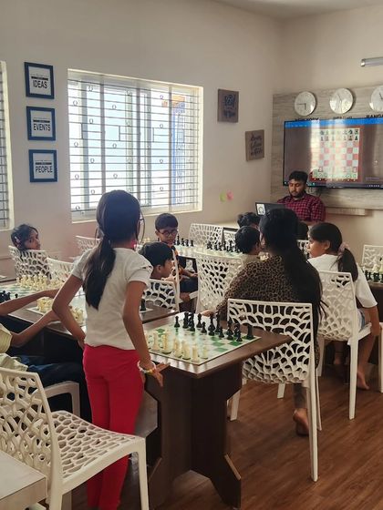 A coach uses a large screen to demonstrate a chess position to the class. We blend traditional board play with modern technology to enhance the learning experience for our students.