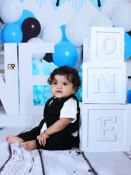 A baby boy sits next to "ONE" blocks in a Boss Baby-themed setup. The cool color palette and props like baby bottles create a unique and humorous first birthday shoot.