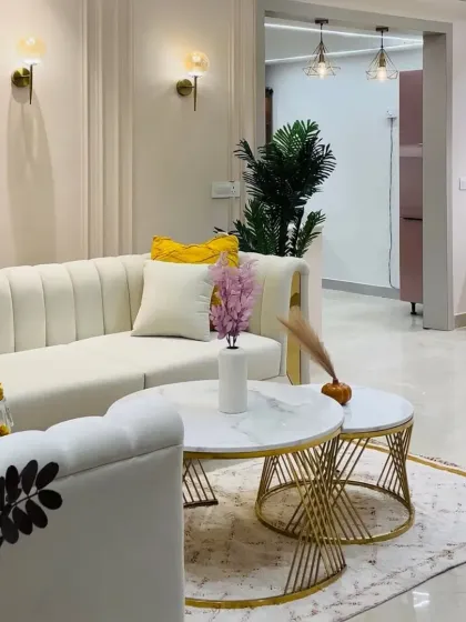 A bright and cheerful living room design. The white sofa with yellow accent pillows, gold-legged coffee tables, and elegant wall sconces create a fresh and glamorous feel.
