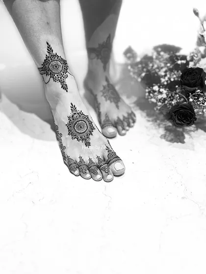 Bridal mehendi isn't just for the hands. This artistic black and white photo captures a symmetrical foot design, featuring a central mandala with detailed patterns extending to the toes, ensuring the bride is adorned from head to toe.