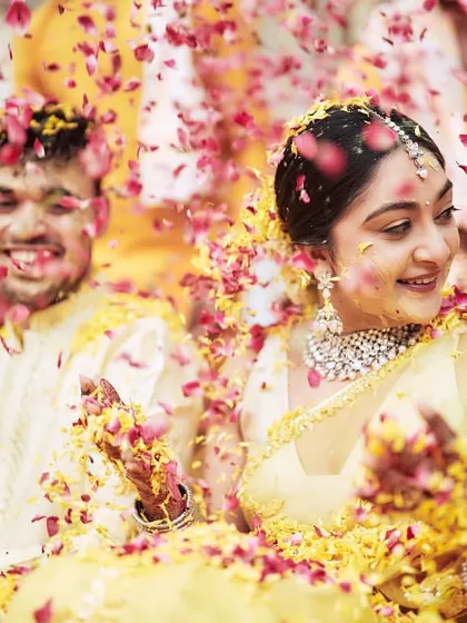 The couple smiling as they are showered with pink and yellow petals, perfectly matching their outfits and the decor.