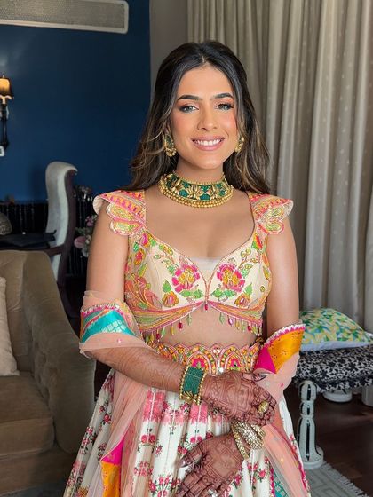 A happy bride at her Mehendi ceremony, her hair styled in a beautiful braided half-updo with soft waves.