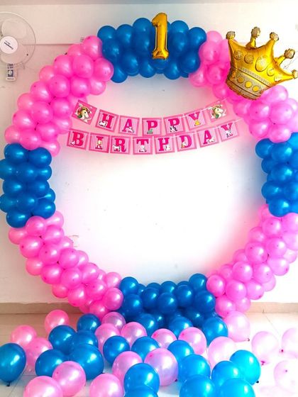 A simple first birthday balloon ring in bright pink and blue. The decoration includes a crown foil balloon and a 'Happy Birthday' banner.