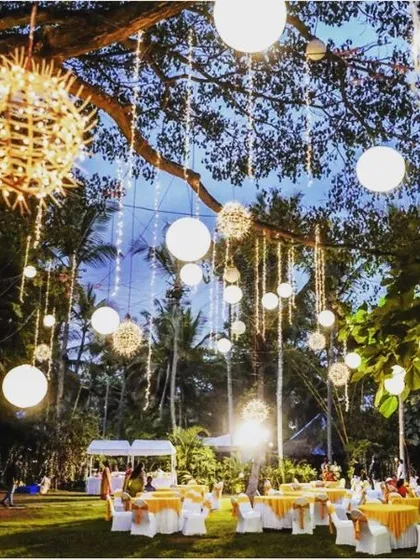The warm glow of the lanterns and lights creates a festive and inviting atmosphere for an outdoor wedding reception.