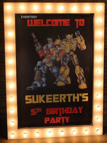 The welcome sign for the Transformers 5th birthday party, designed like a movie poster with a bright marquee light border. It features Optimus Prime and Bumblebee, ready for action.