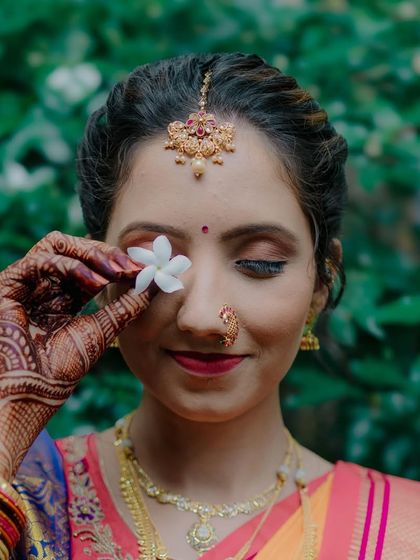A creative bridal portrait where the bride, Siddhi, holds a small white flower over one eye, adding a touch of artistry and nature to the shot.