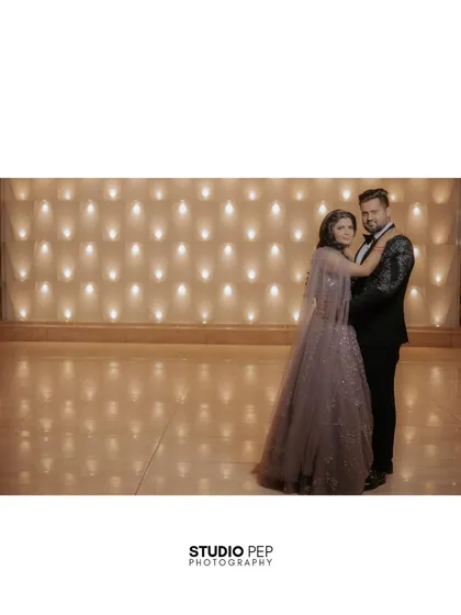 A wide shot of the couple dancing, showcasing the grand, warmly lit venue and the graceful flow of the bride's gown.
