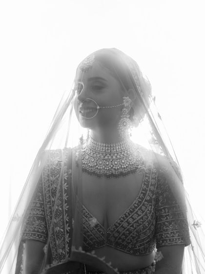 A dreamy, high-key black and white bridal portrait. The light filtering through her veil creates an ethereal and angelic effect.