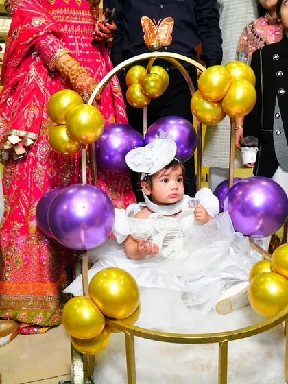 The birthday girl makes a grand entrance in a specially decorated cart adorned with purple and gold balloons, perfectly matching the butterfly theme of the party.