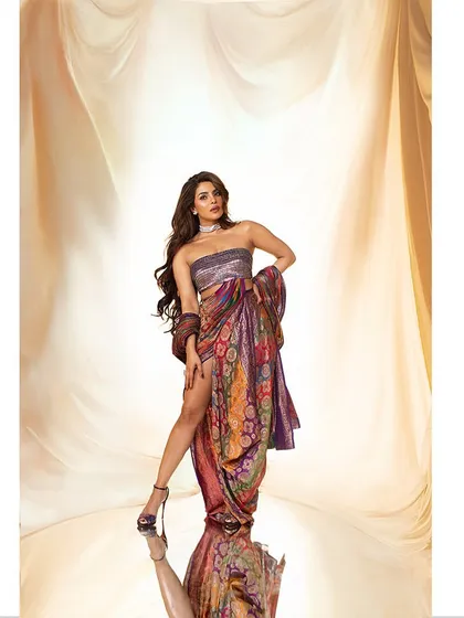 A studio portrait of Priyanka Chopra, styled in a draped, multi-patterned ensemble. The lighting is designed to sculpt her form and highlight the rich textures of the fabric, creating a regal and powerful image.