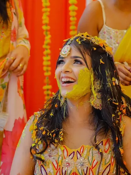 A bride's face lights up with a huge smile as she gets playfully covered in turmeric and flowers during her Haldi ceremony.